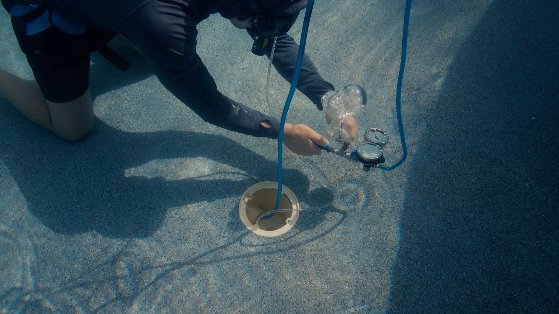 Person underwater adjusts a gauge connected to a buoy in a pool.