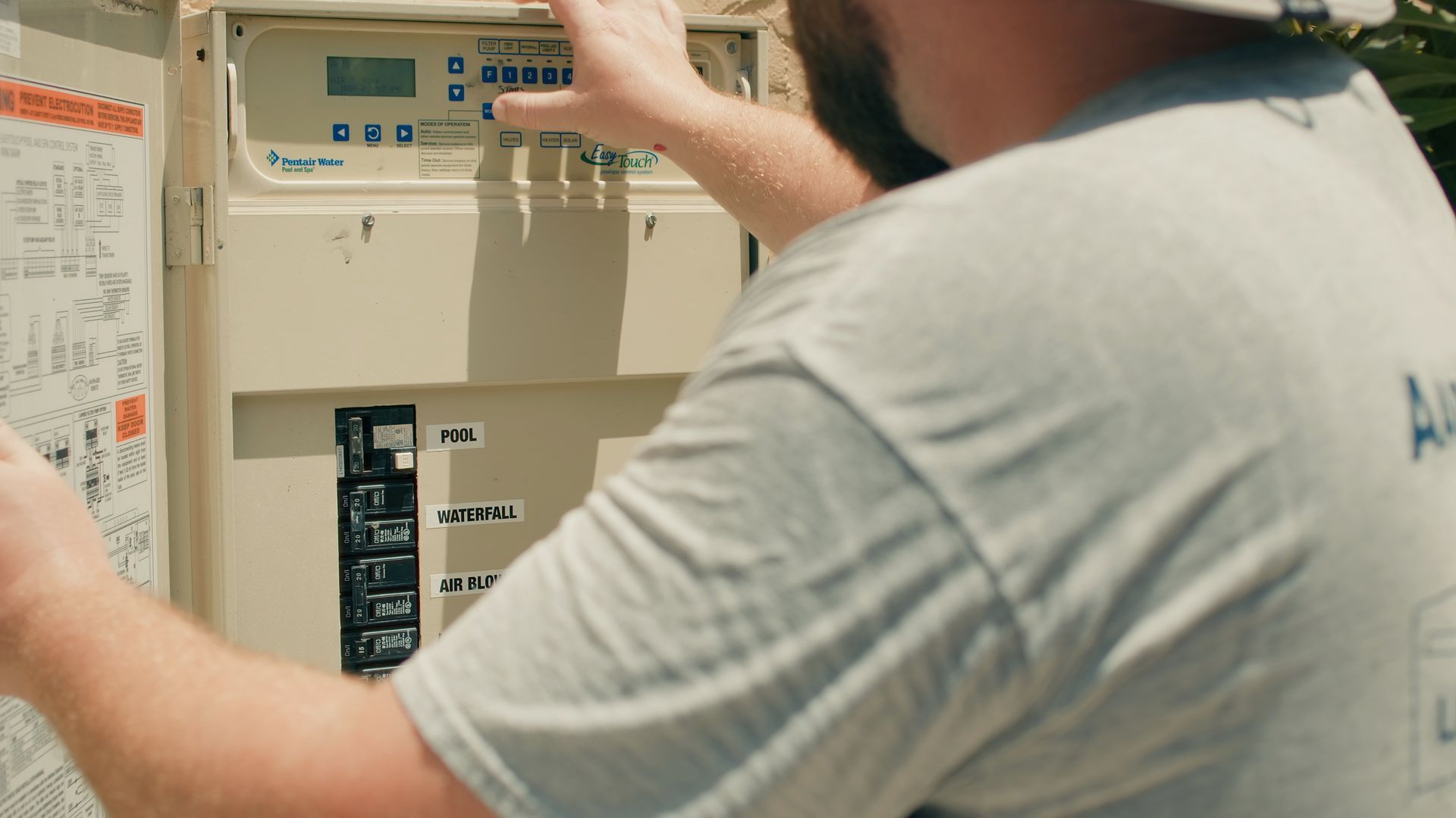 Person in grey shirt working on an electrical panel outside.
