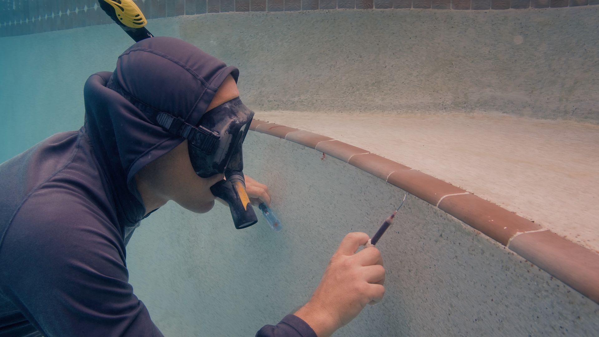 Person with snorkel cleaning a pool with a brush.