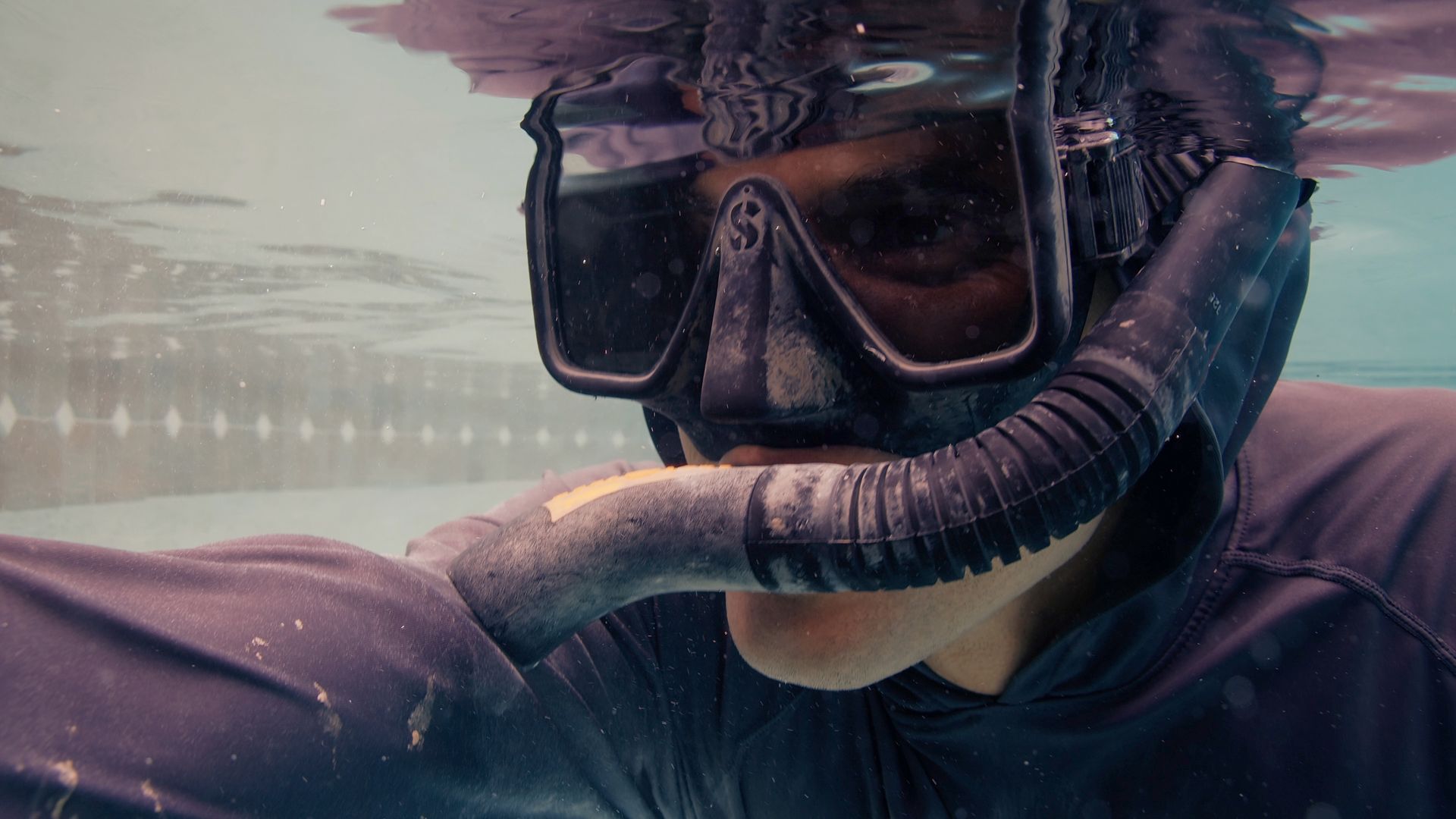 Person underwater wearing a snorkeling mask and snorkel, looking forward.