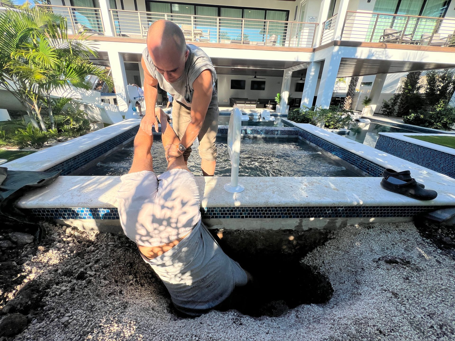 Two people work on a water feature with white tile. One leans into the water, the other stands above.