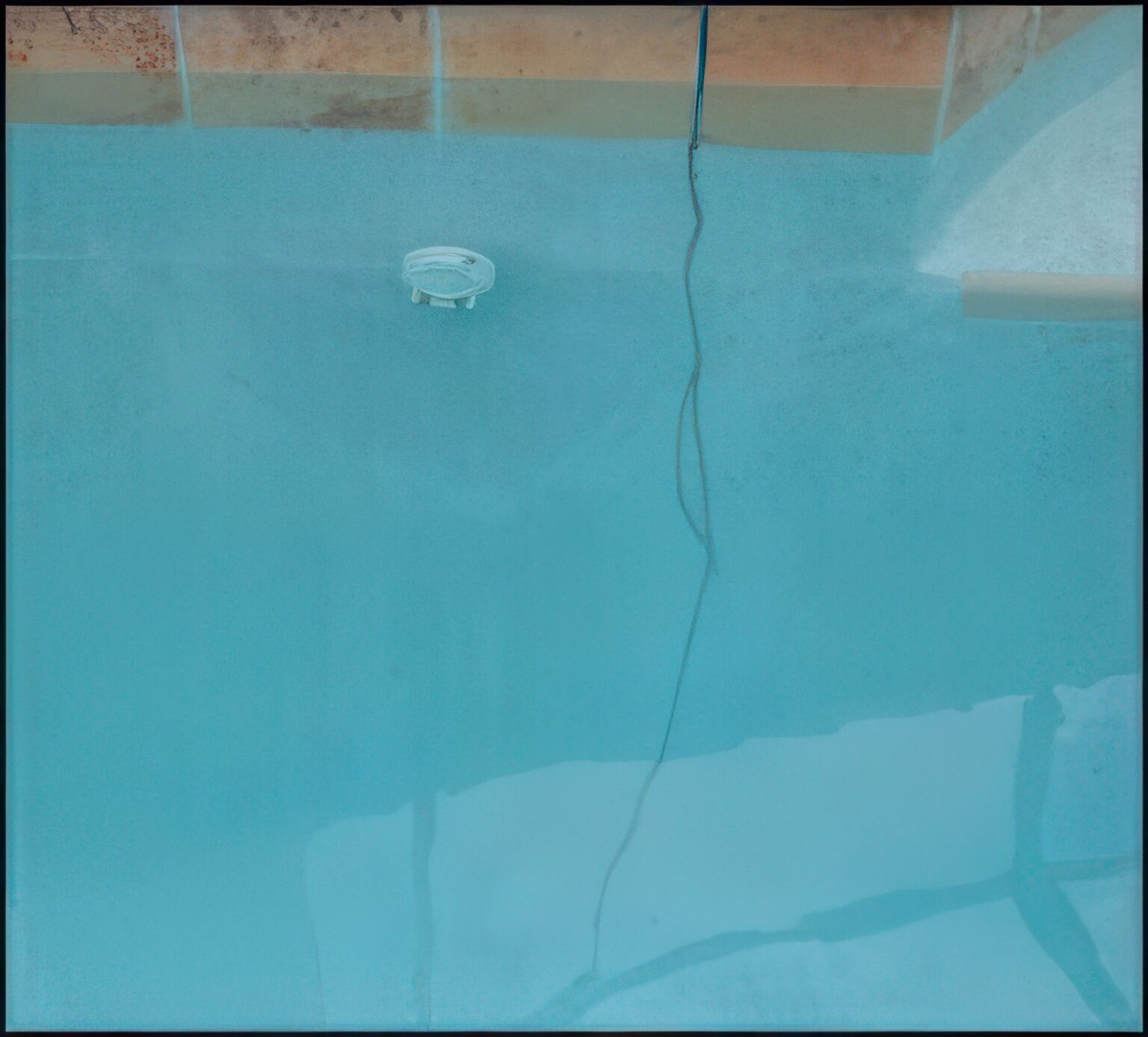 Blue swimming pool with an underwater light fixture and a power cord.