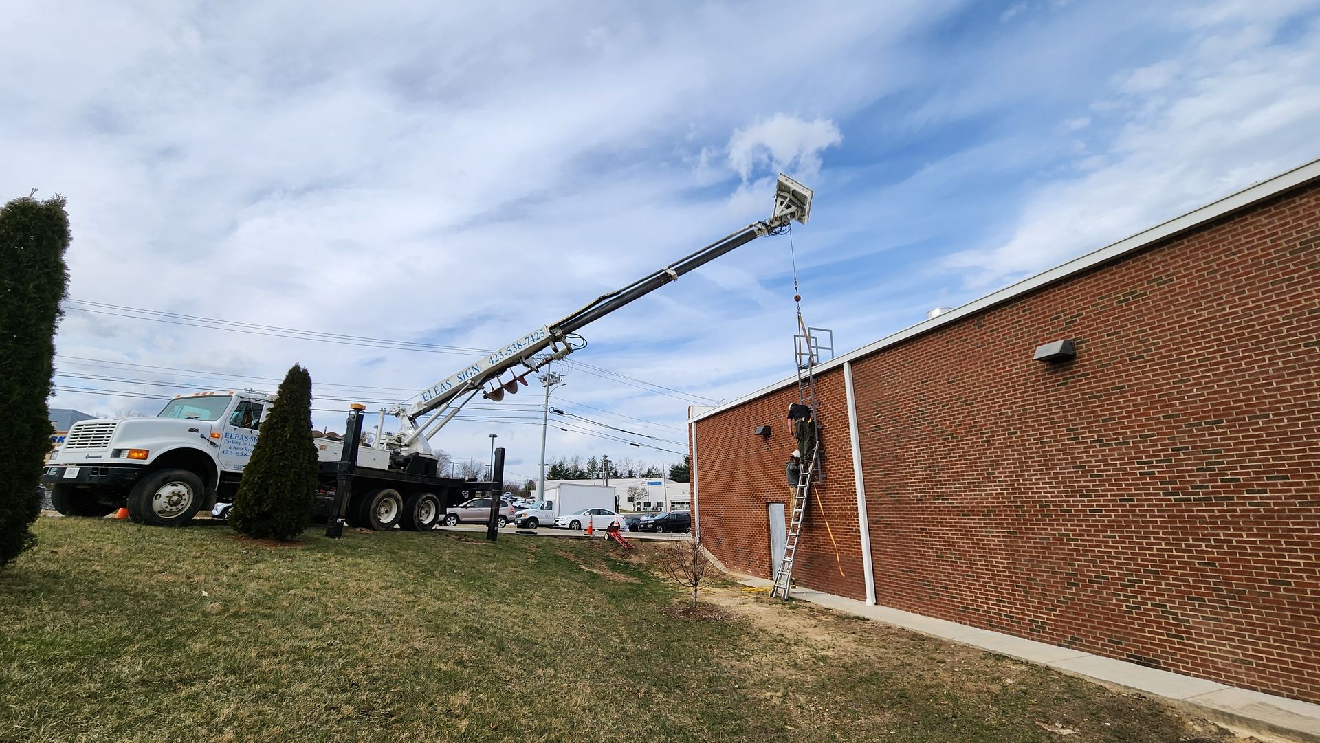 A white truck with a crane attached to it is parked in front of a brick building.