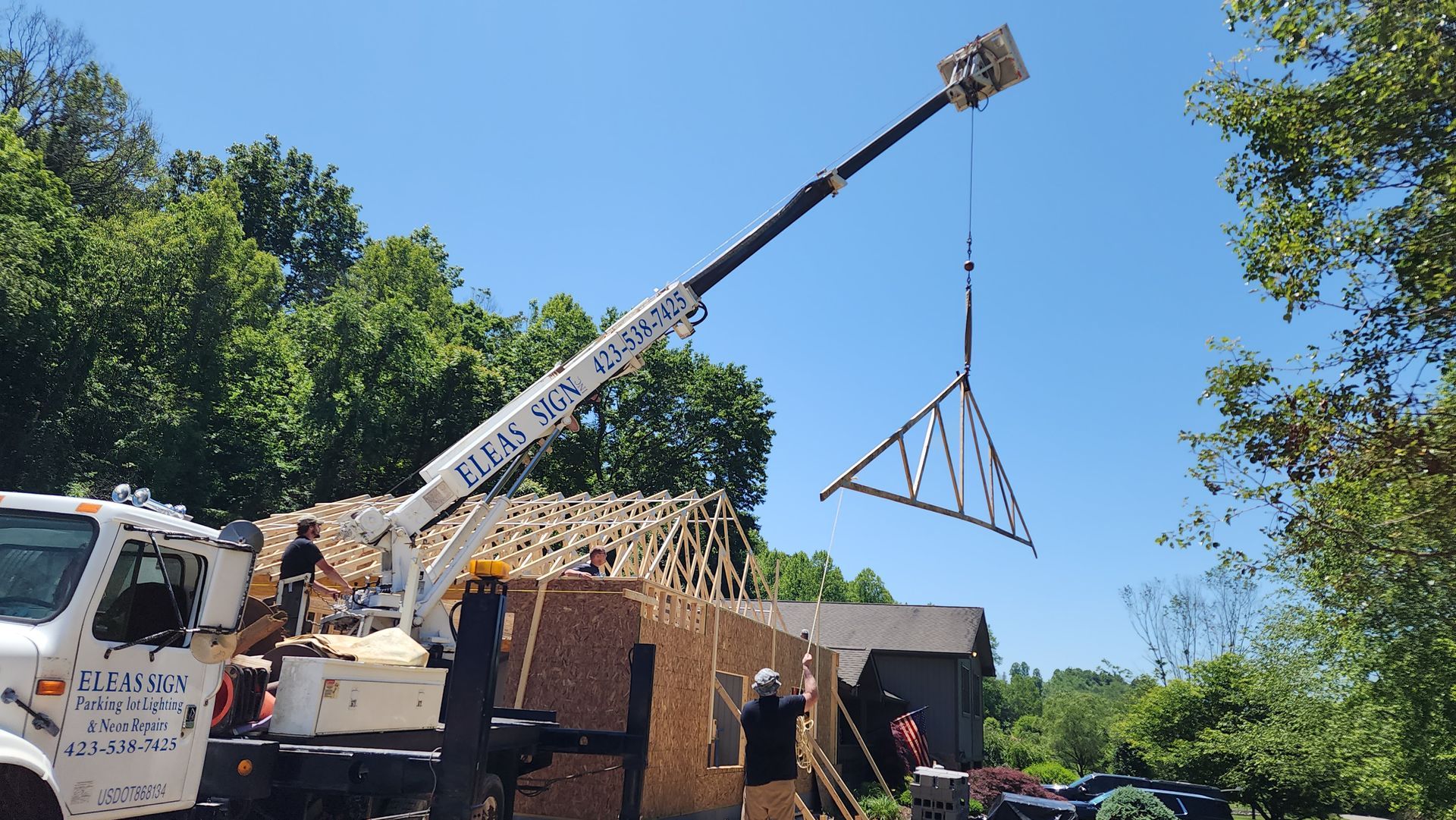 A crane is lifting a truss over a house under construction.