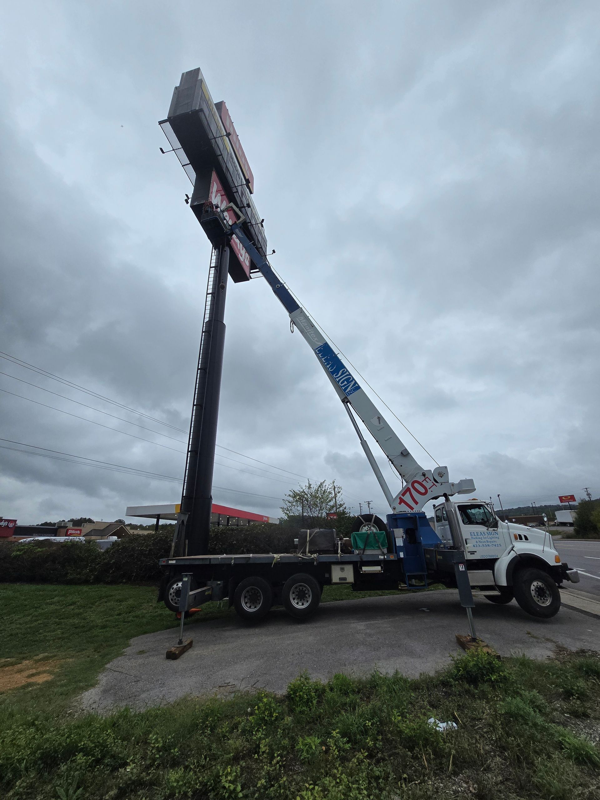 A truck with a crane attached to it is lifting a large sign.