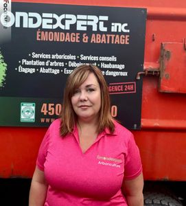 Une femme portant une chemise rose se tient devant un panneau indiquant Ondexpert Inc.