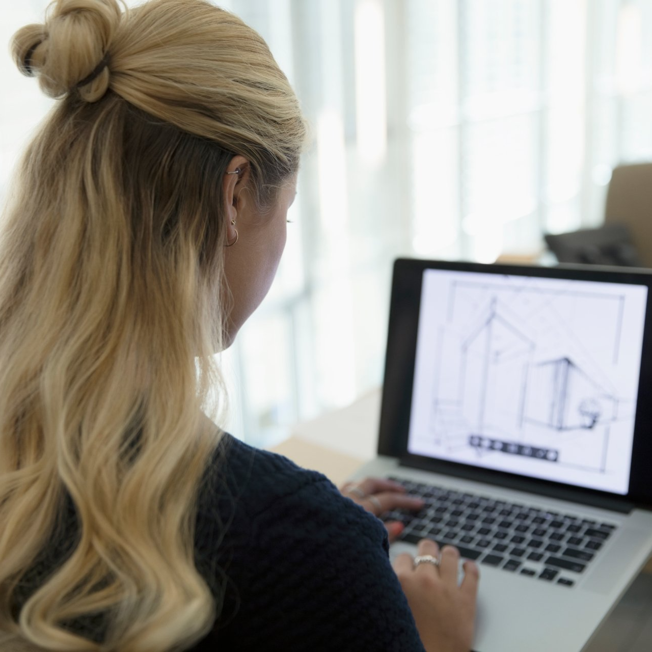 Blonde, female architect viewing digital blueprints on laptop