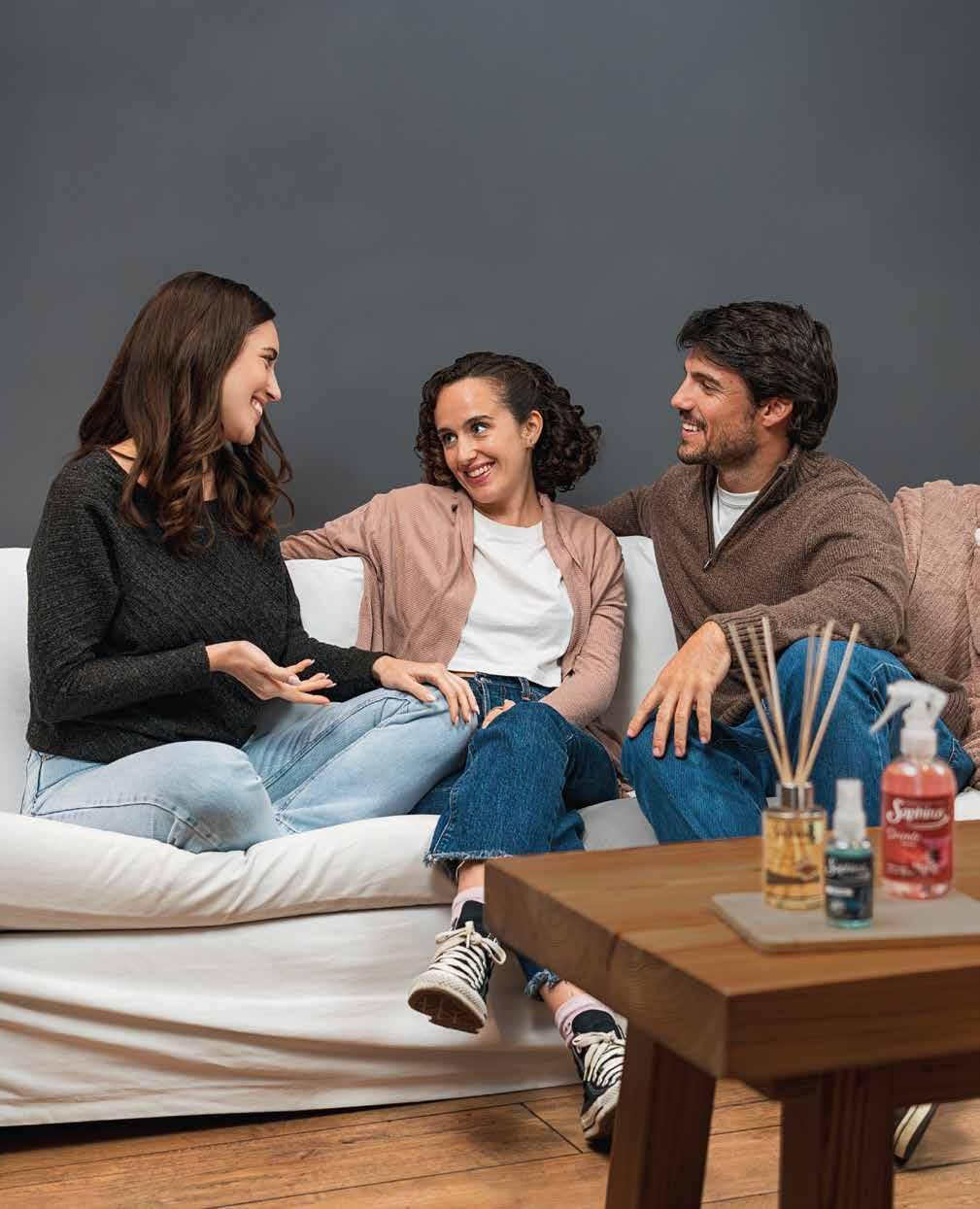 Tres personas sonriendo en un sofá con productos de fragancia para el ambiente en una mesa de café.