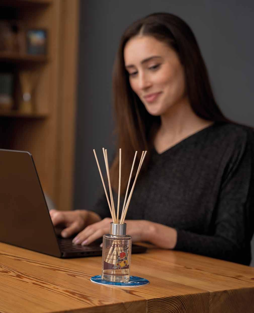 Mujer usando una laptop con un difusor de varillas sobre la mesa. Sonriendo, trabajando en una oficina en casa.