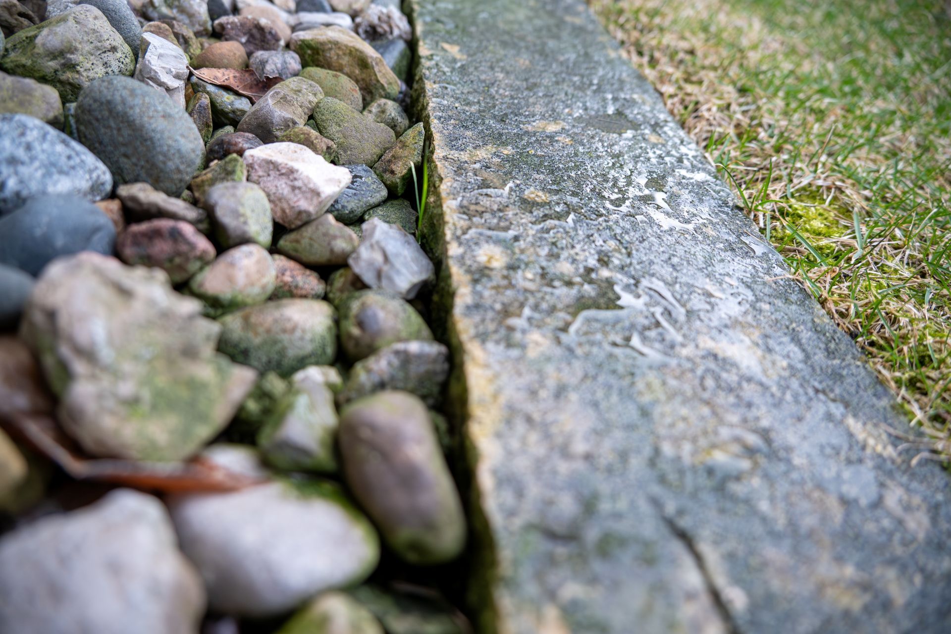Close-up of stones beside a weathered concrete curb with grass along the edge