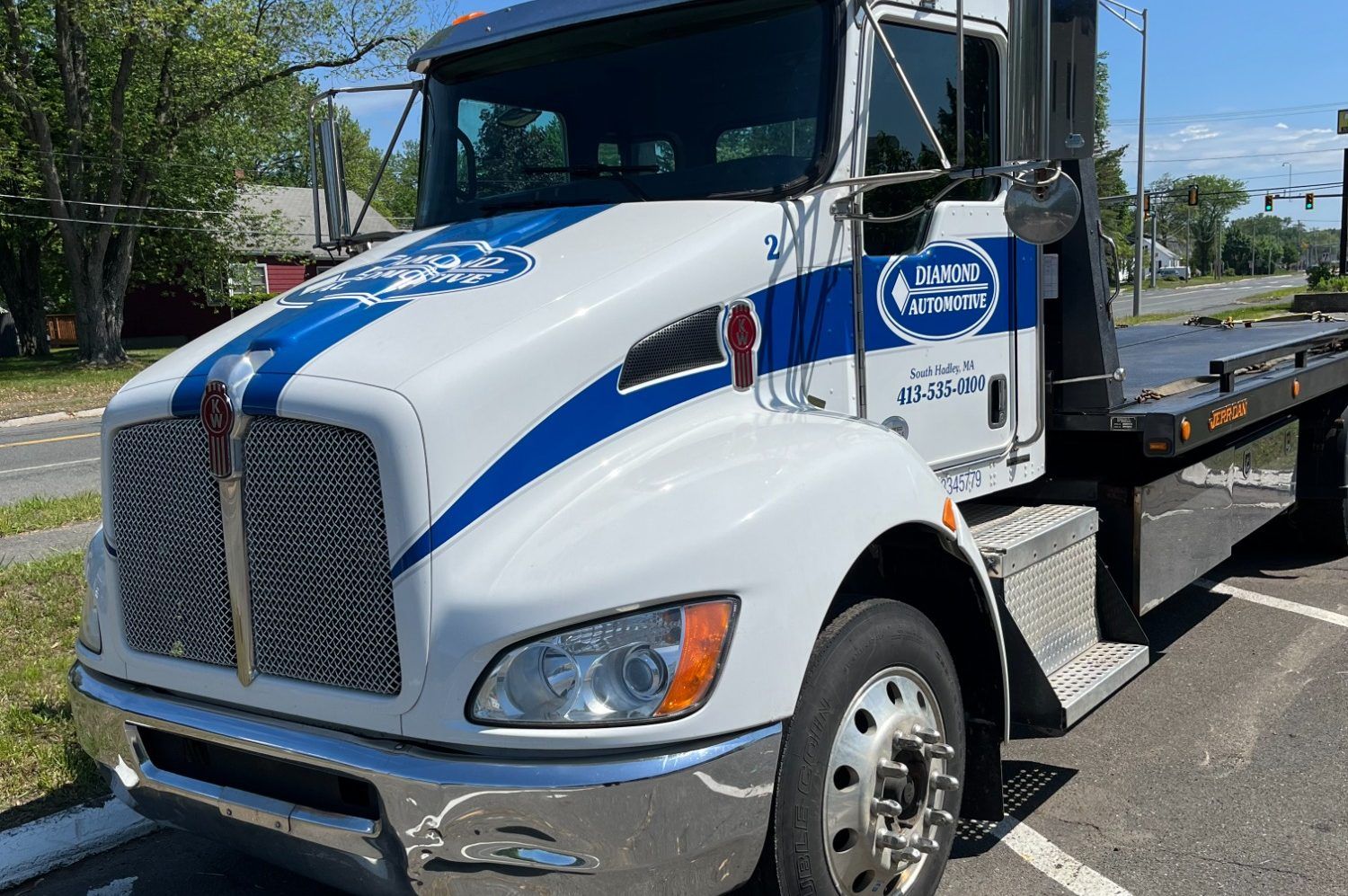 White and blue tow truck with company logo parked next to a road | Diamond Automotive
