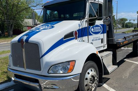 White and blue tow truck with company logo parked next to a road | Diamond Automotive