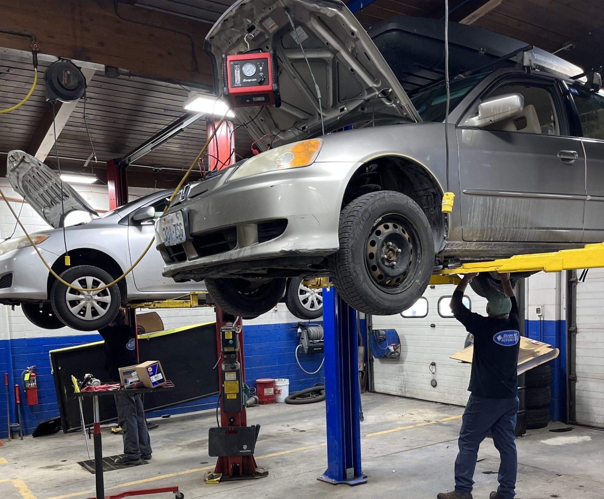 Cars on lifts in a garage; a mechanic works on the car under a diagnostic light | Diamond Automotive