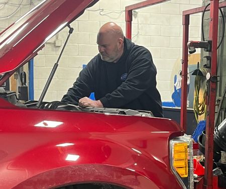 Mechanic in a garage working on a red truck with the hood open | Diamond Automotive