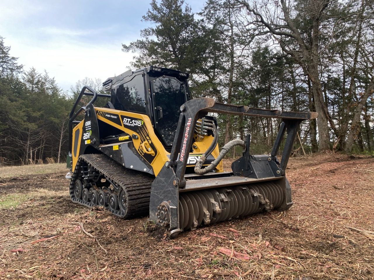 Yellow and black forestry mulcher on tracks in a wooded area.