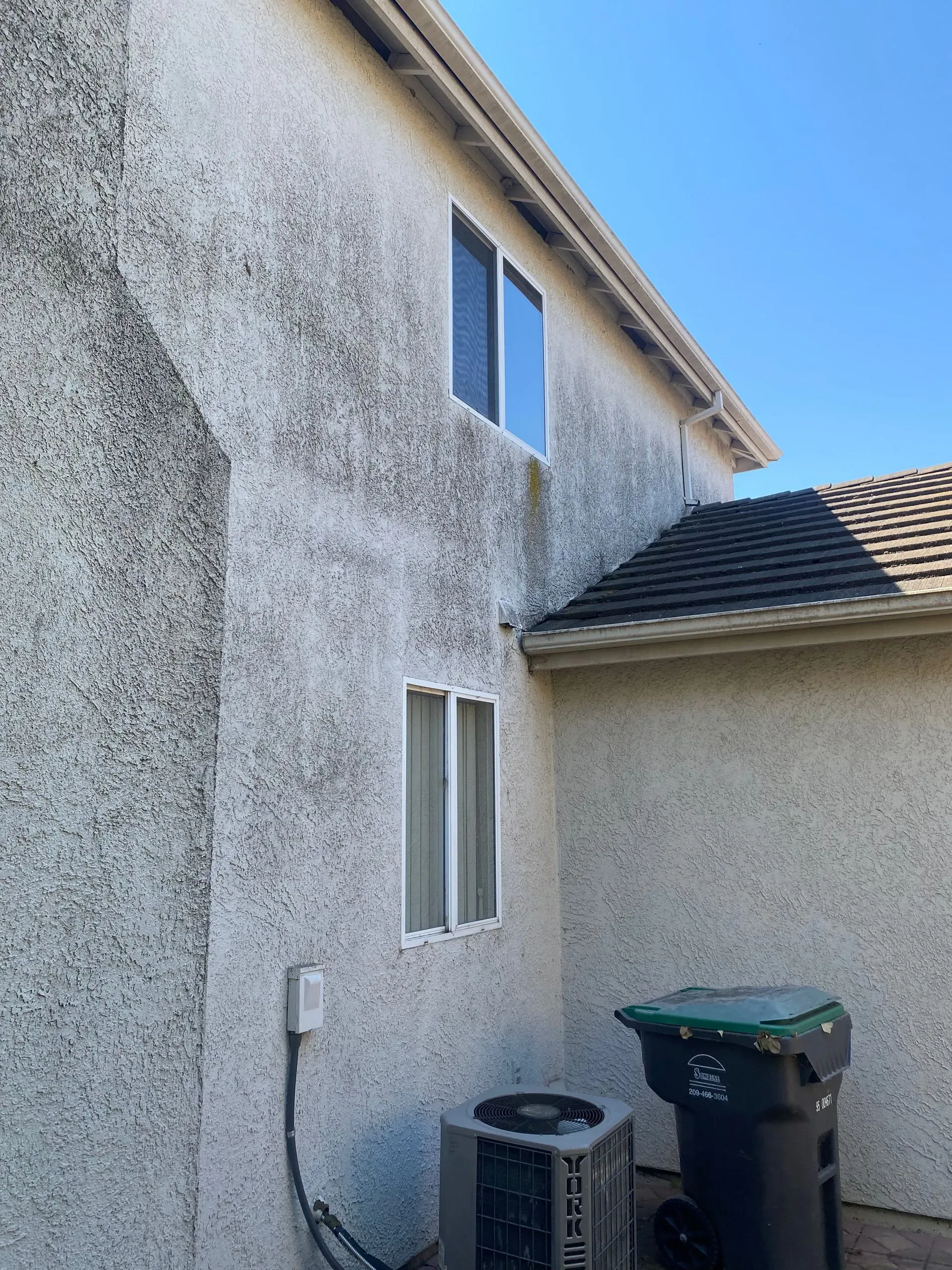A white house with a green trash can and an air conditioner on the side.