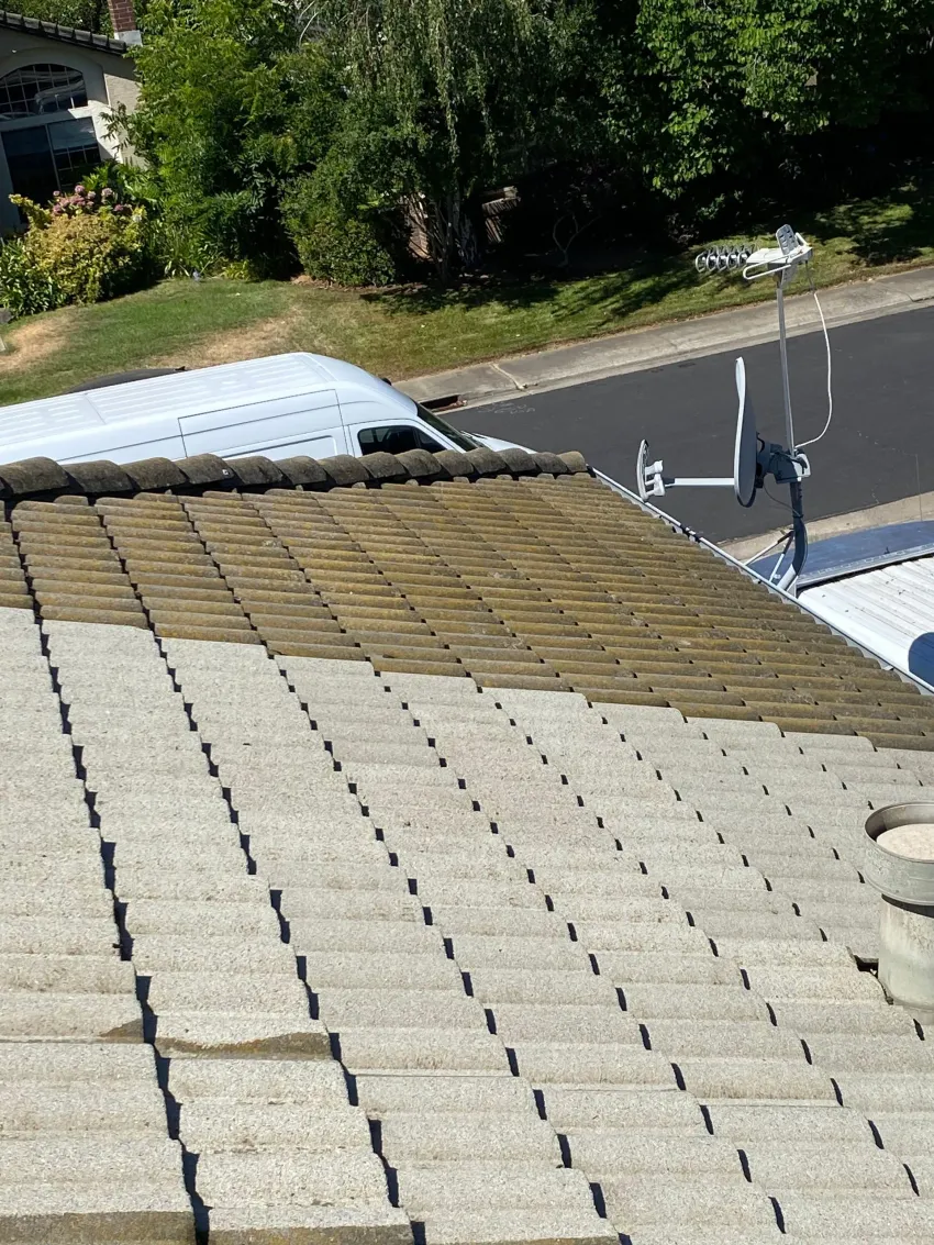 A man is cleaning the roof of a house with a high pressure washer.
