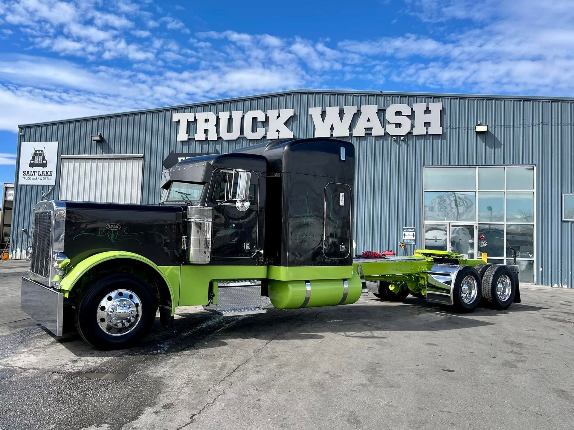 A black and green semi truck is parked in front of a truck wash.