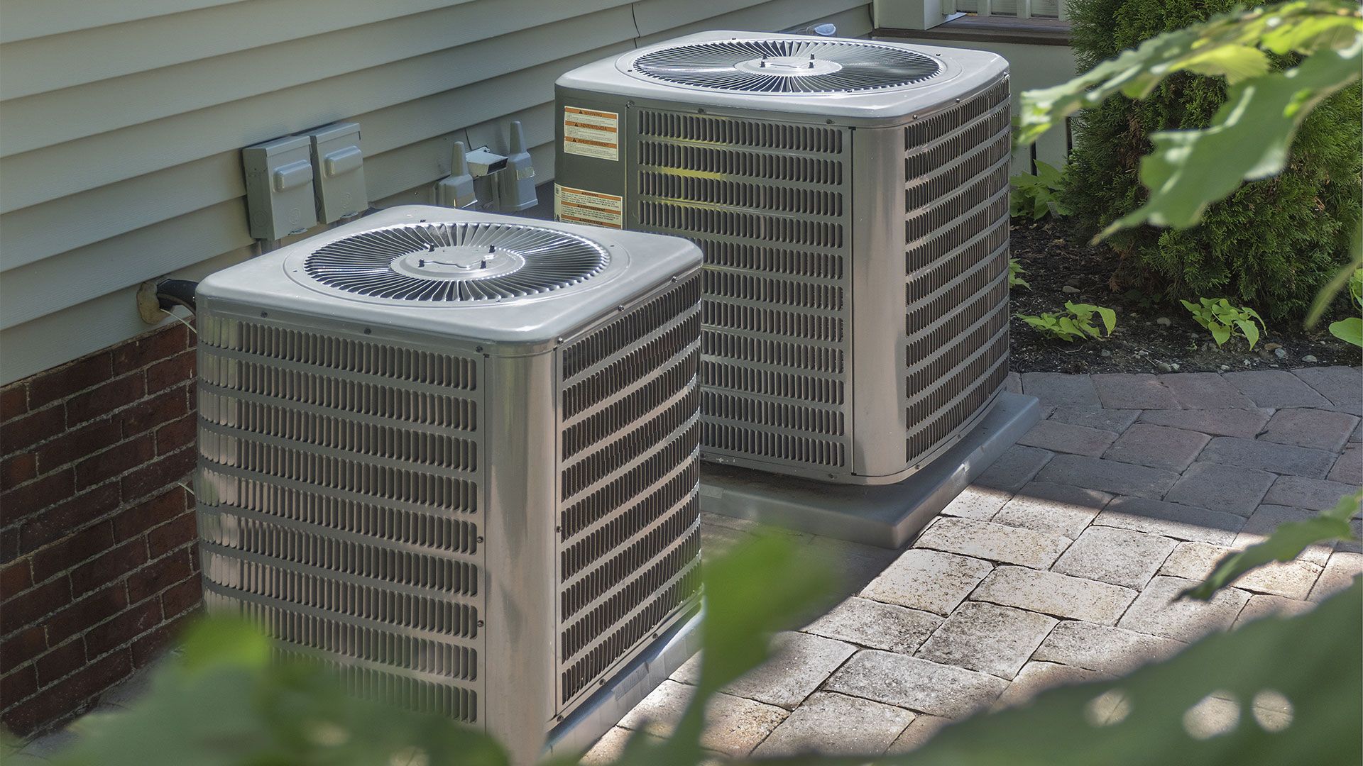 Two air conditioners are sitting on the side of a house.
