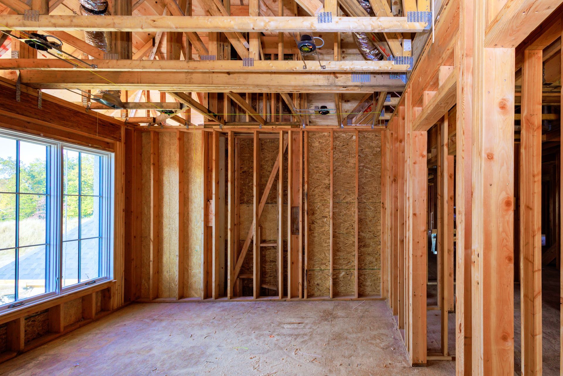 Unfinished wooden room framing with exposed beams and a large window letting in daylight.
