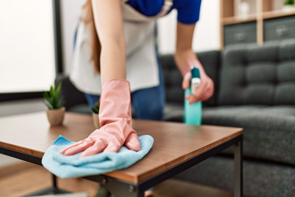 A woman in pink gloves is cleaning a wooden table in a living room.