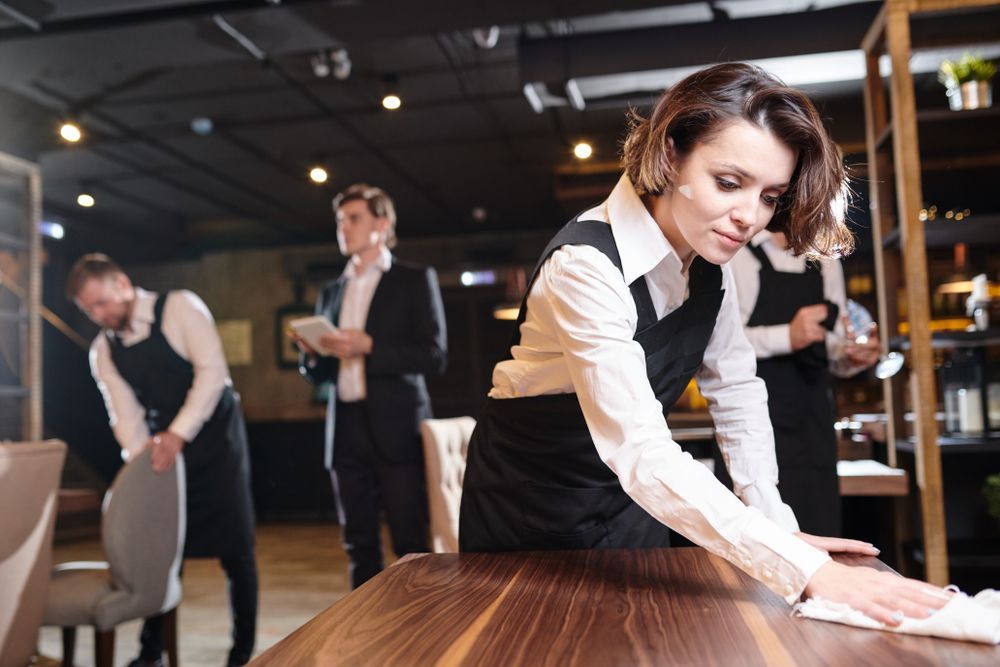 A woman is cleaning a wooden table in a restaurant.