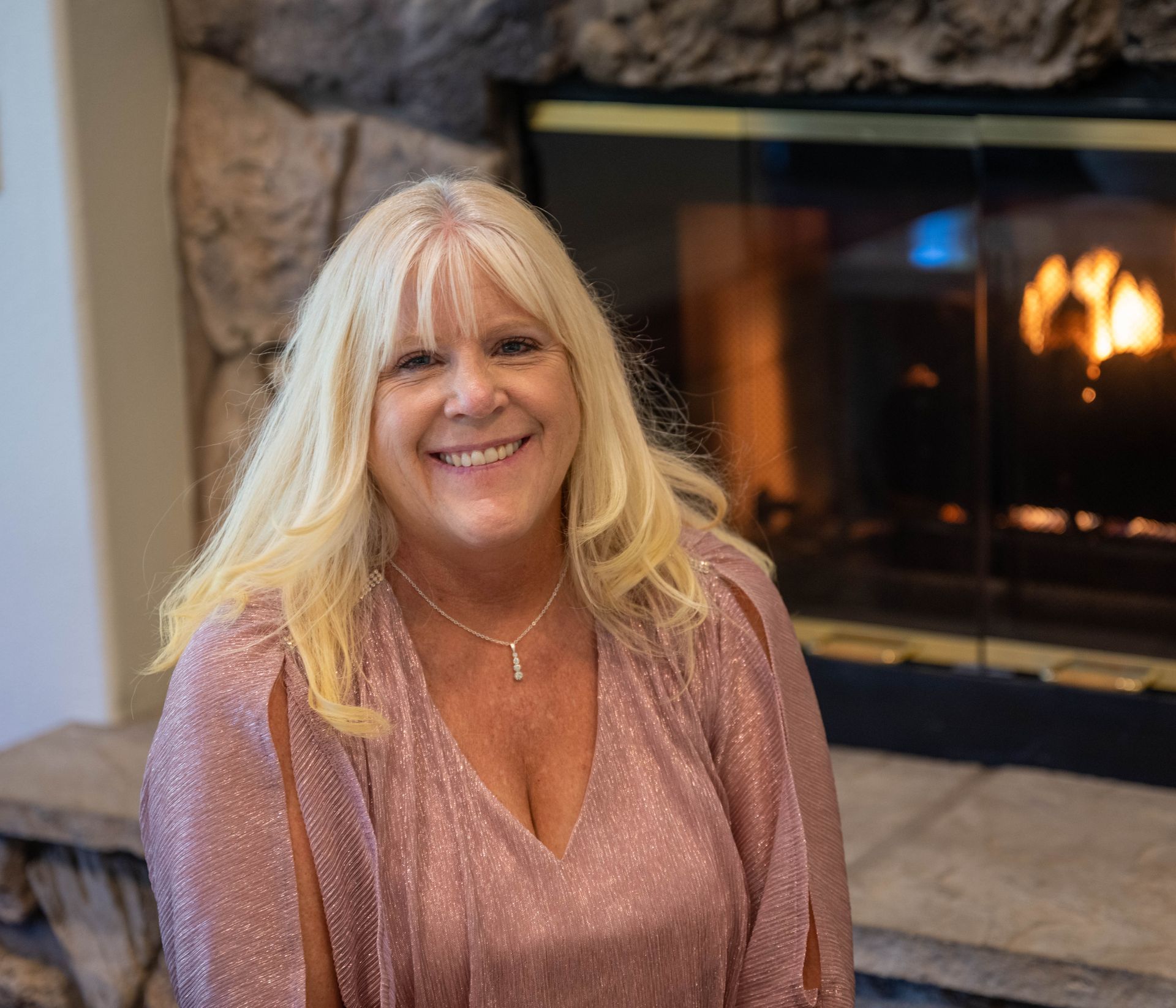 Kim Silverman is sitting in front of a fireplace smiling.