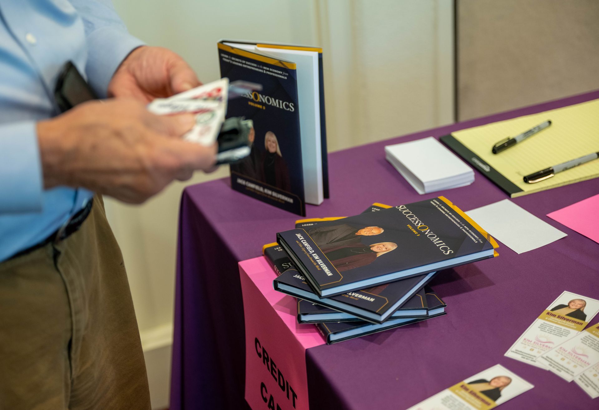 A man is holding a piece of paper in front of a table with books on it.