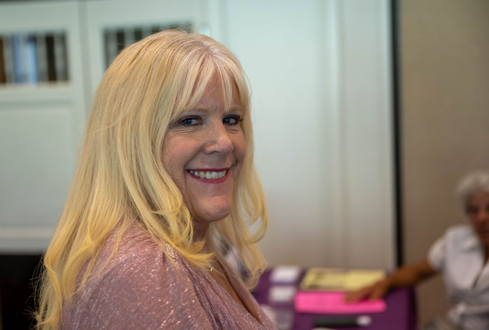 Kim Silverman with blonde hair is smiling for the camera while sitting at a table.