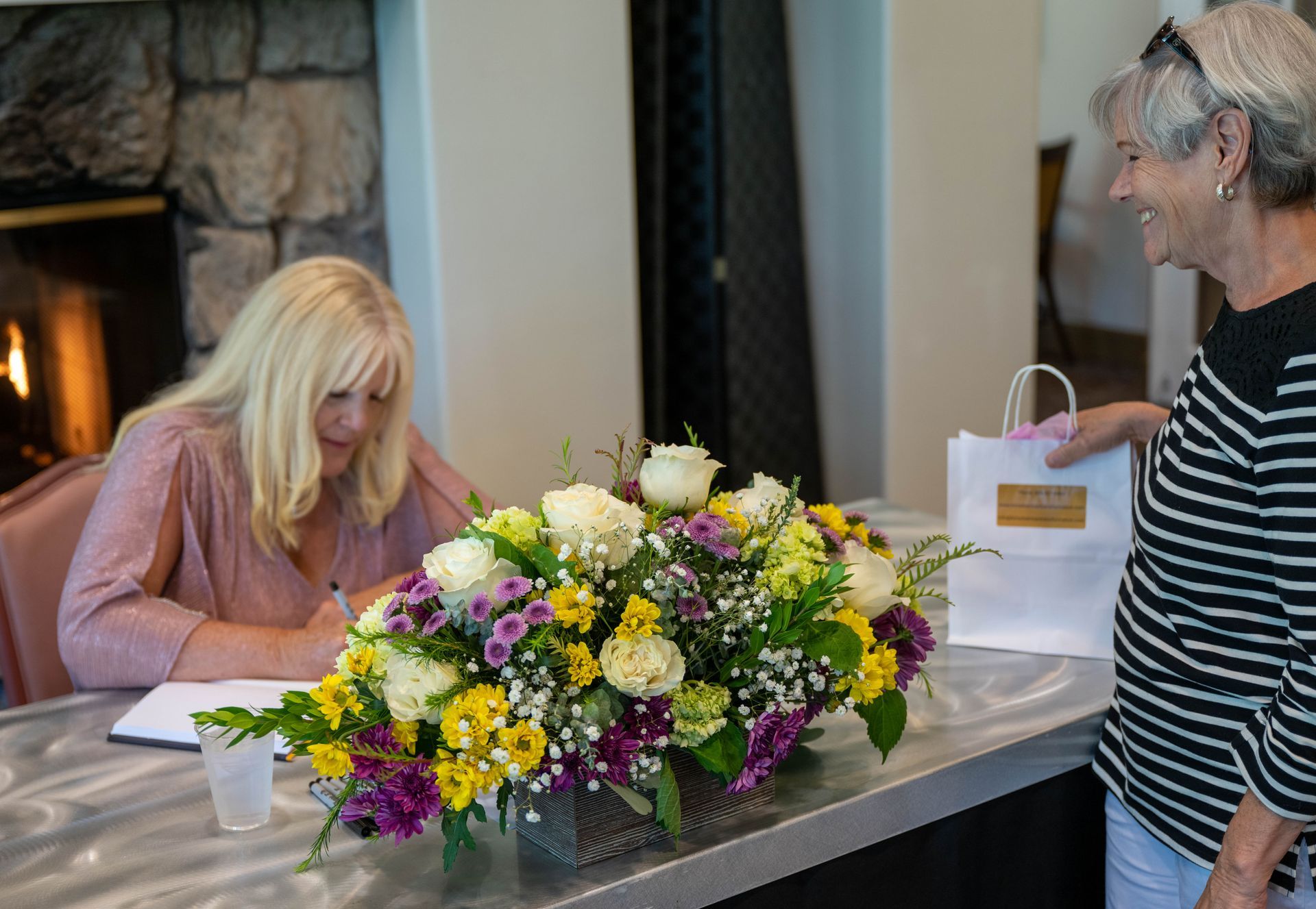 Kim Silverman is signing a book next to a vase of flowers.