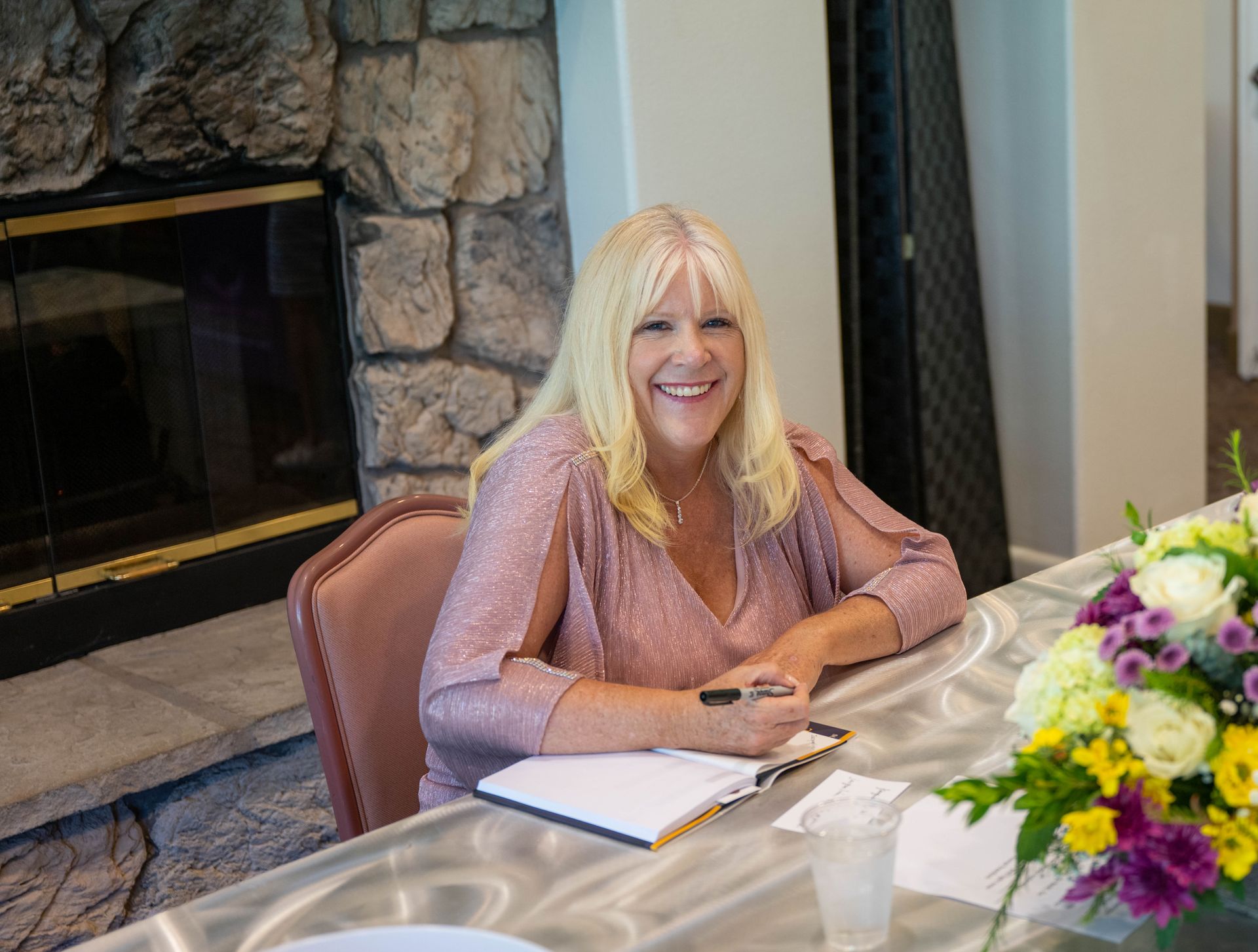 Kim Silverman is sitting at a table with flowers and a SuccessOnomics book.