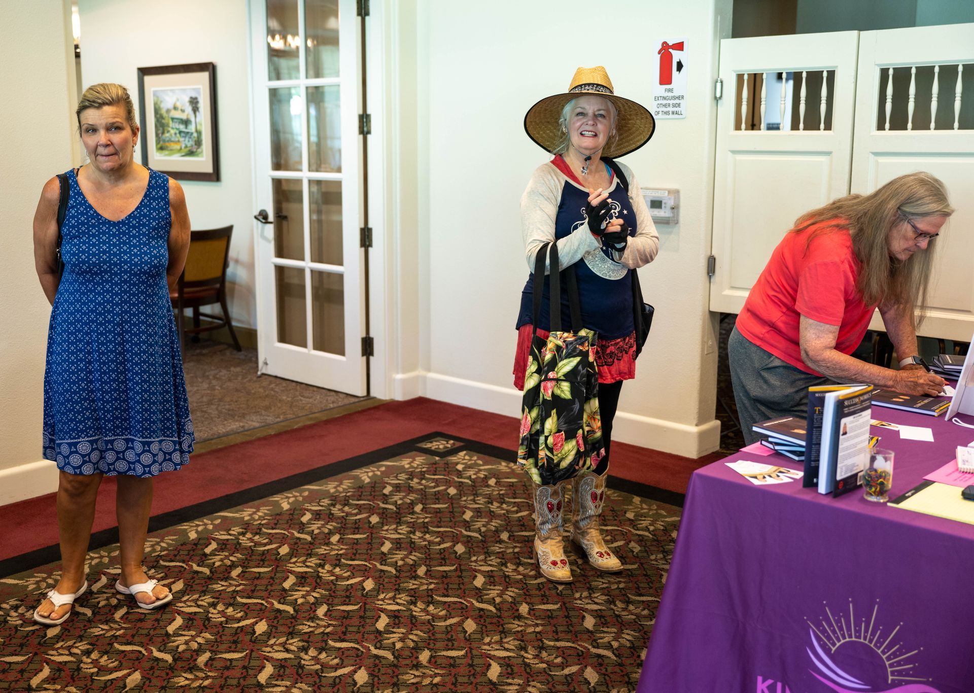 Three women are standing in a room next to a table with a purple table cloth.