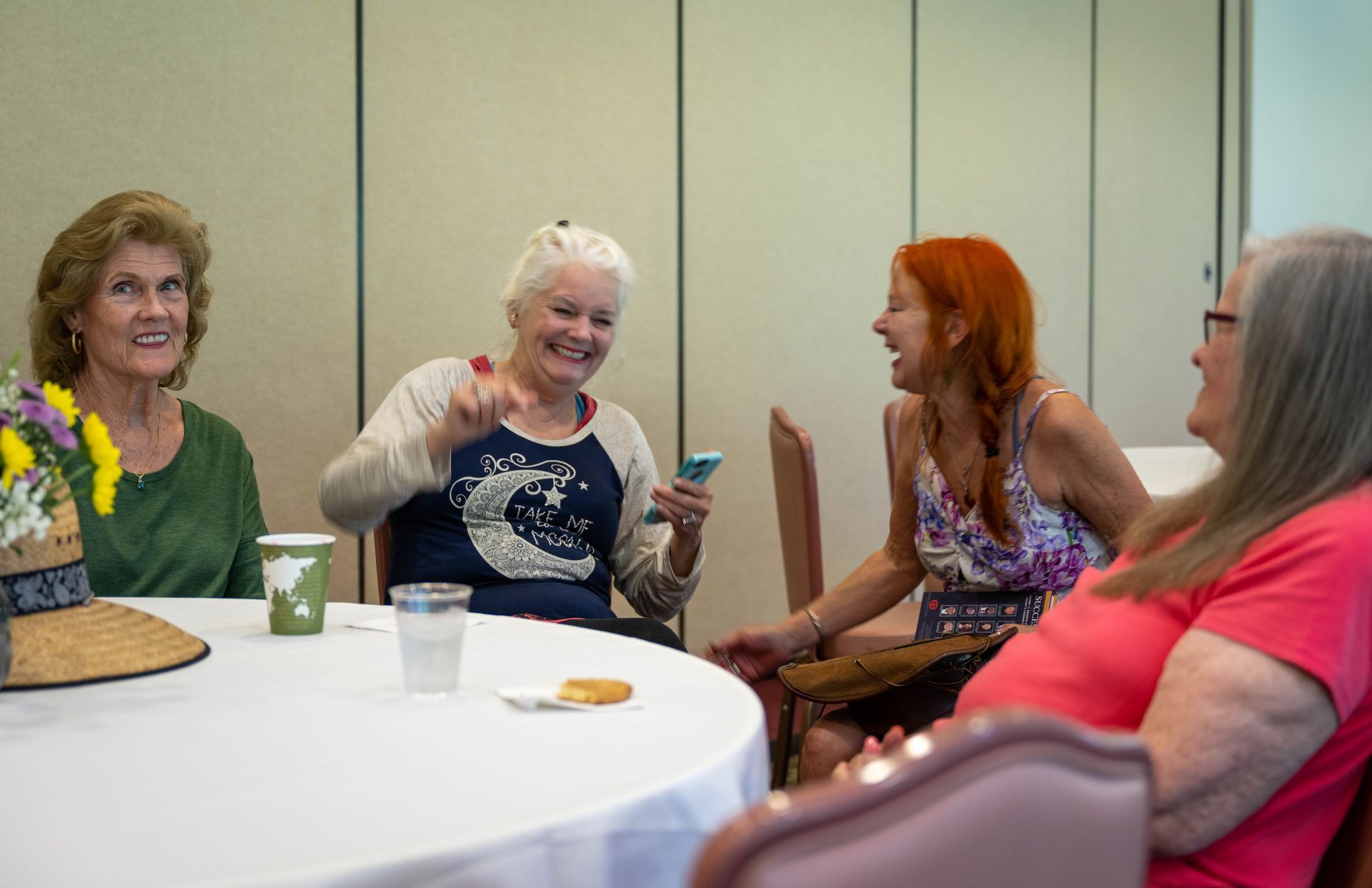 A group of women are sitting around a table talking to each other.