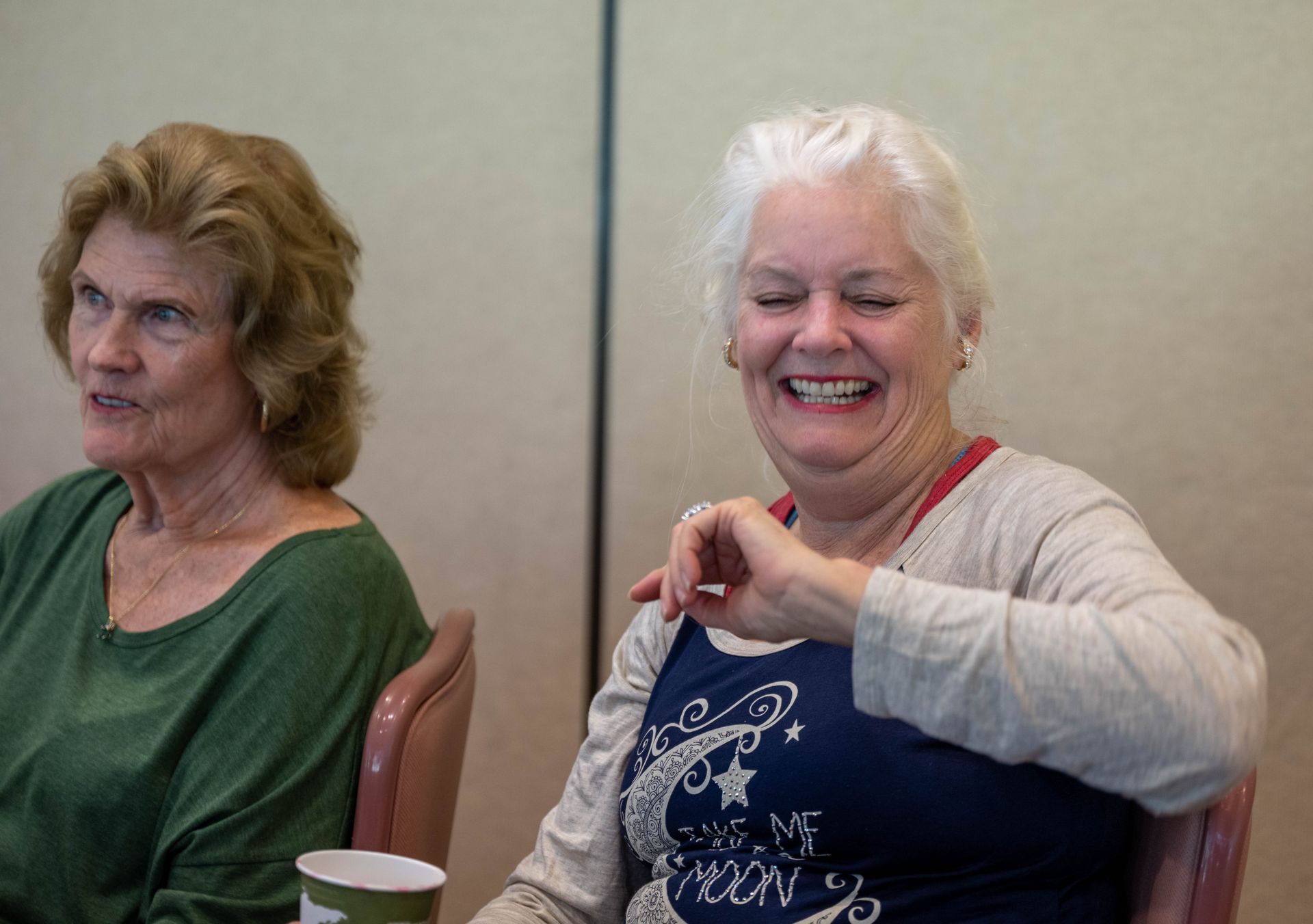 Two older women are sitting at a table and smiling.