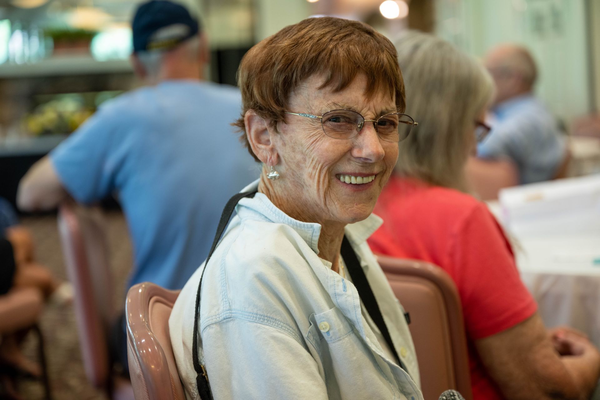 An elderly woman is smiling while sitting at a table with other people.