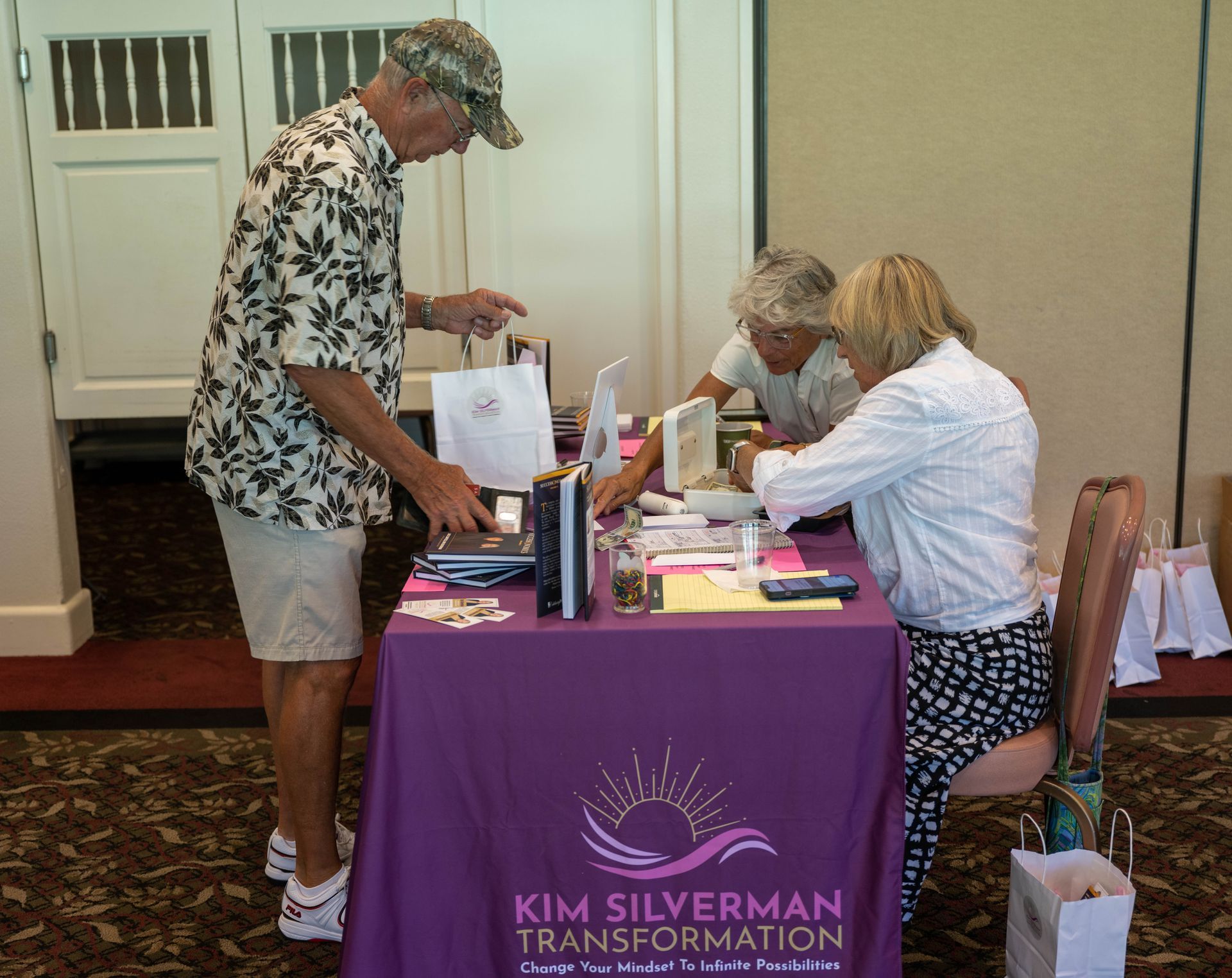 A man standing at a table with a purple table cloth that says kim silverman transformation