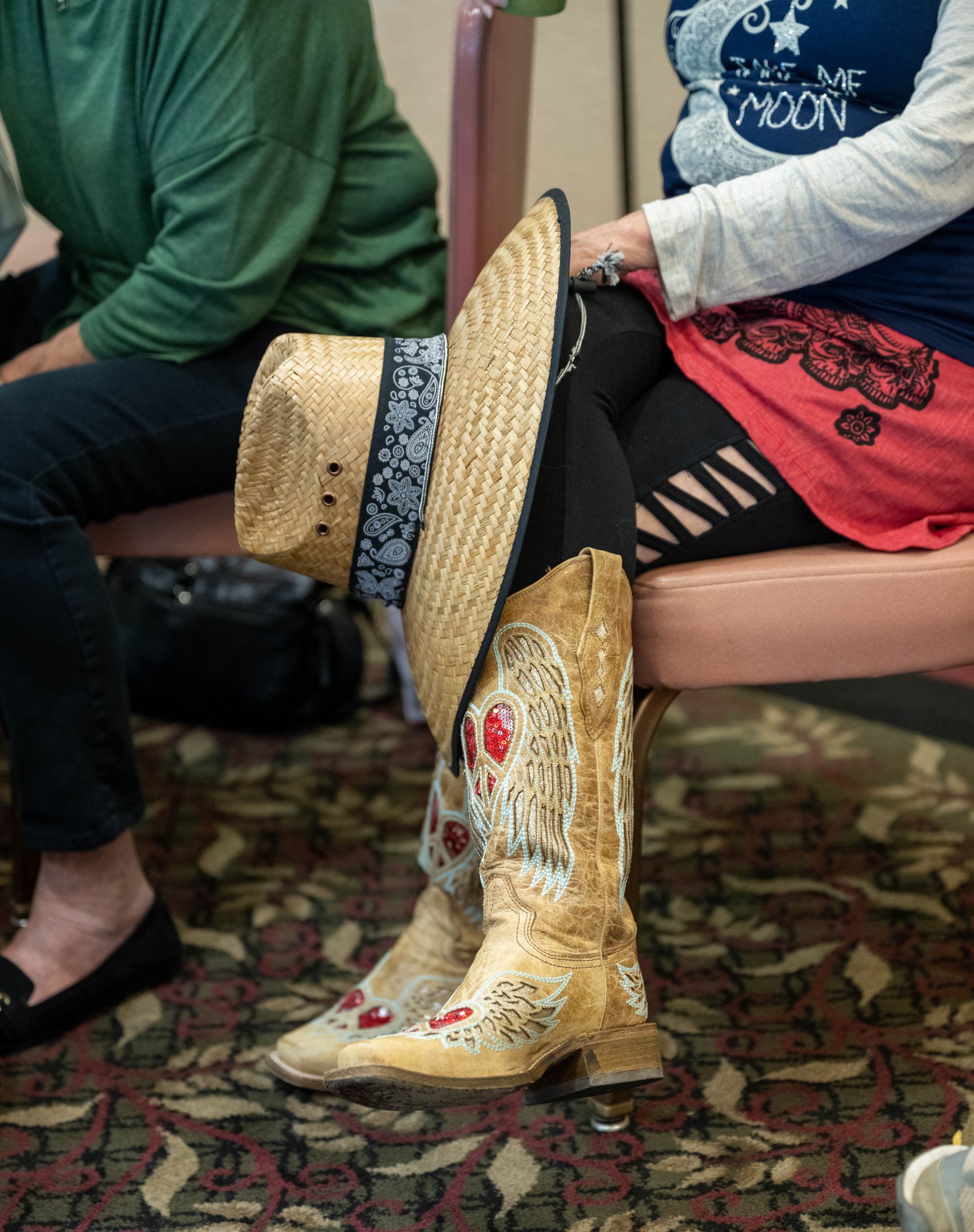 A woman wearing cowboy boots and a hat is sitting in a chair.