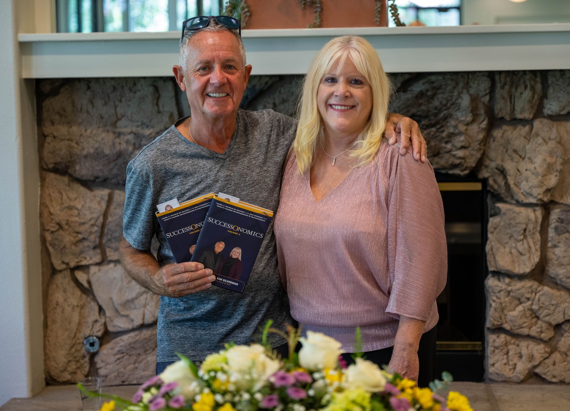 A man and Kim Silverman are posing for a picture in front of a fireplace.