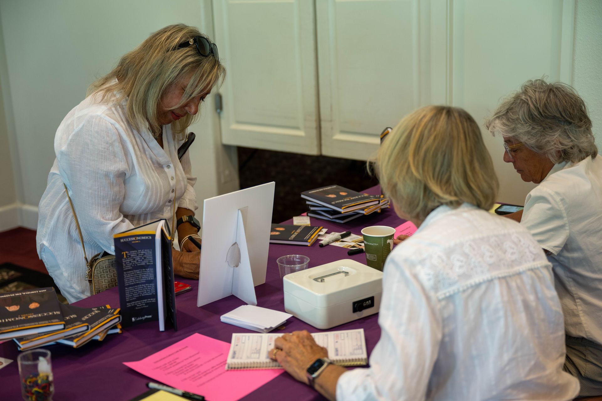 A group of women are sitting at a table looking at a box.