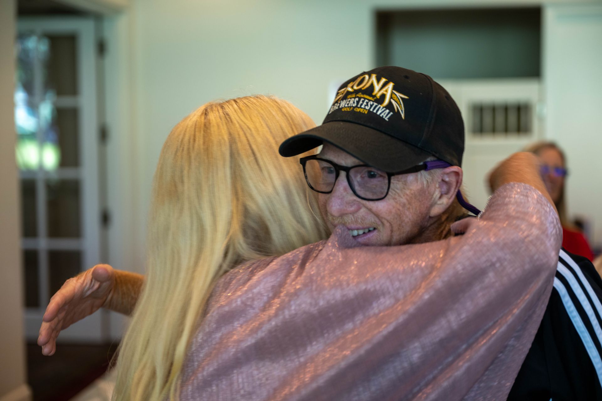 A man wearing a hat and glasses is hugging Kim Silverman.