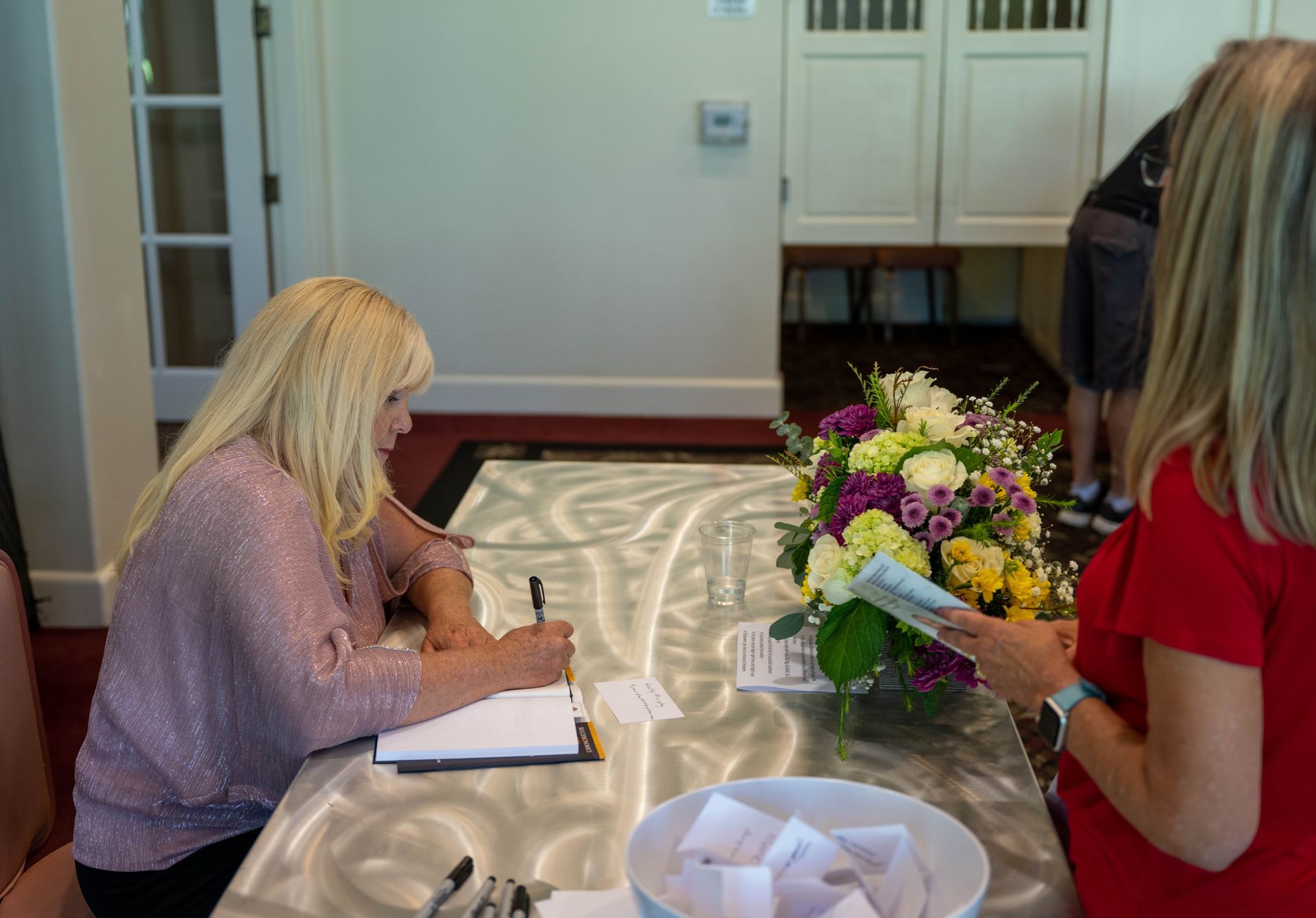 Kim Silverman is sitting at a table autographing a book.