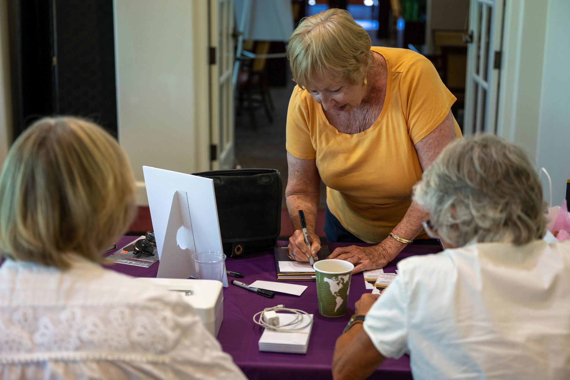 A woman in a yellow shirt is helping another woman write on a piece of paper.