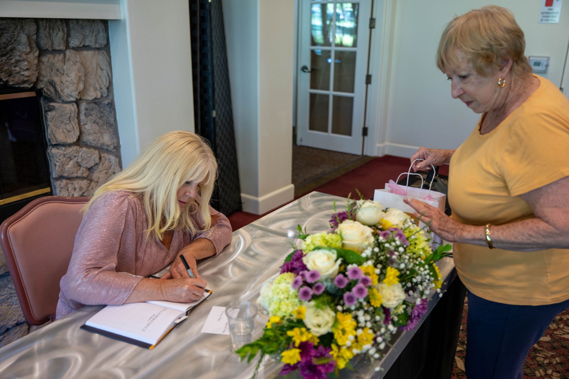 Kim Silverman is signing a book at a table with flowers.