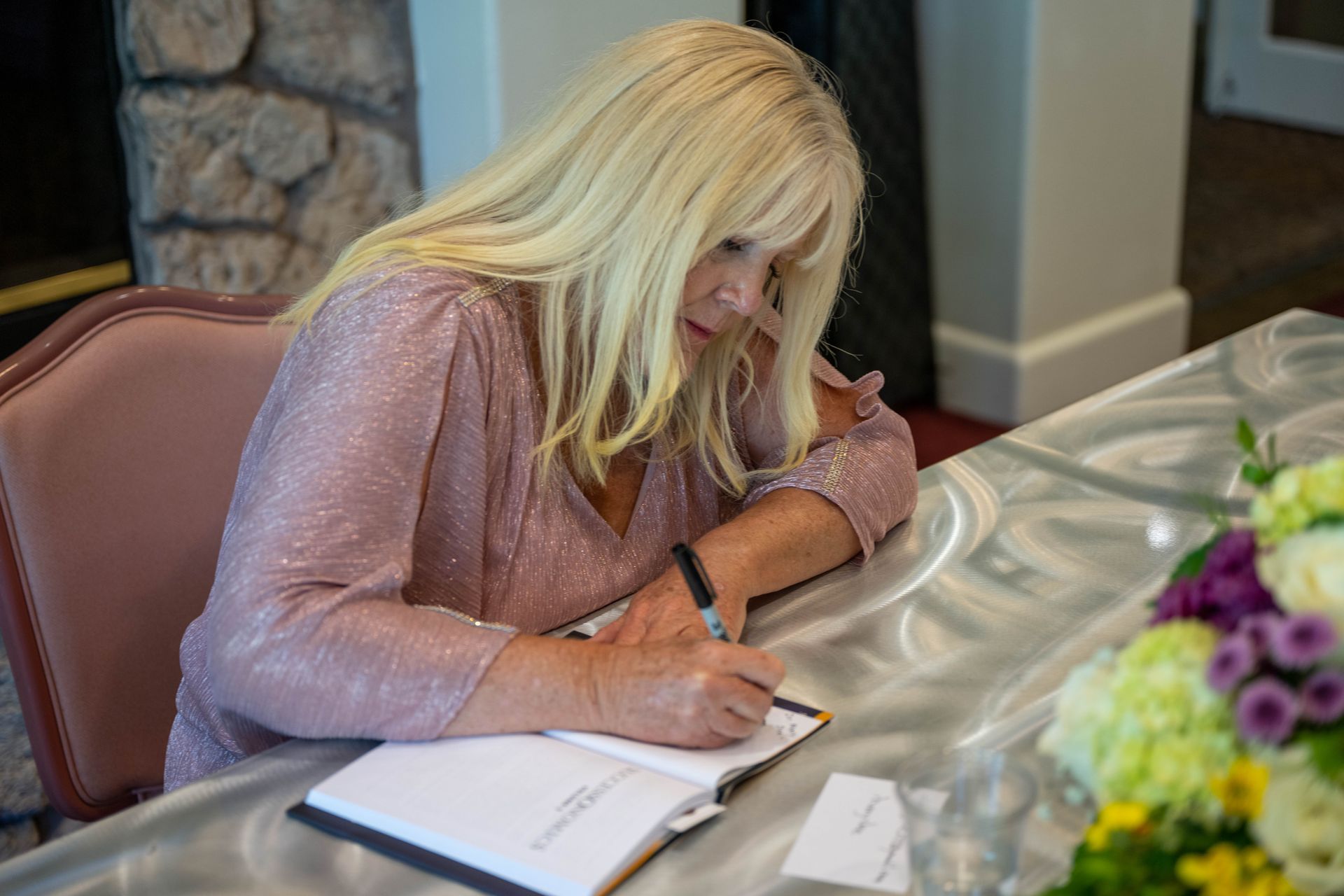 Kim Silverman sitting at a table with flowers signing SuccessOnomics book.