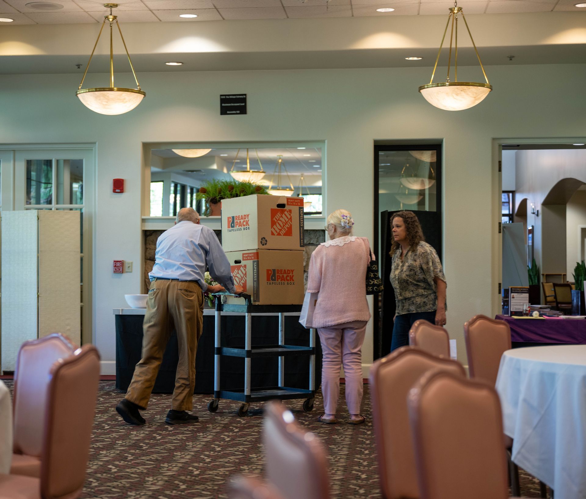 A man pushing a cart with boxes on it in a room with tables and chairs