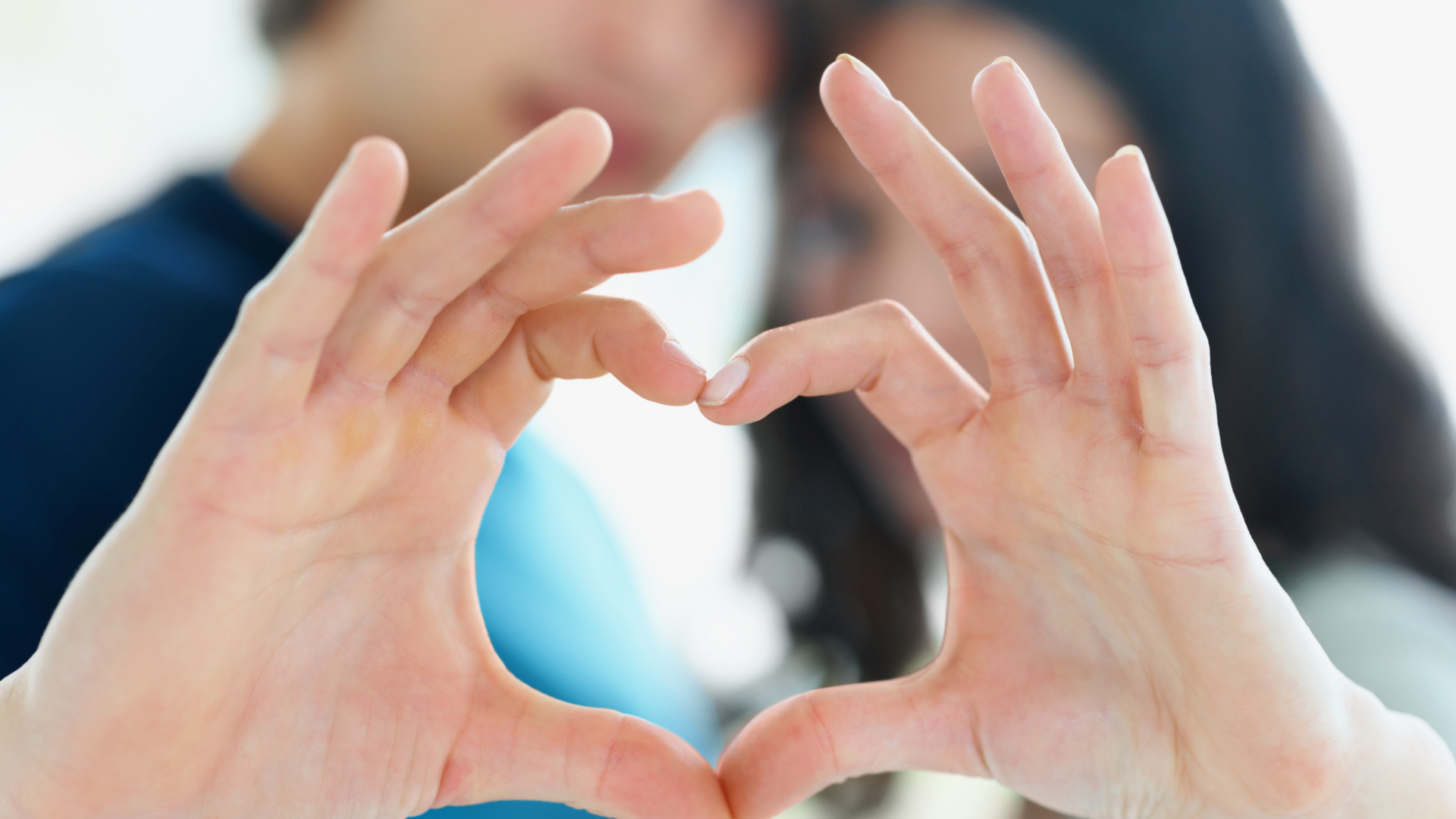 A man and a woman are making a heart shape with their hands.