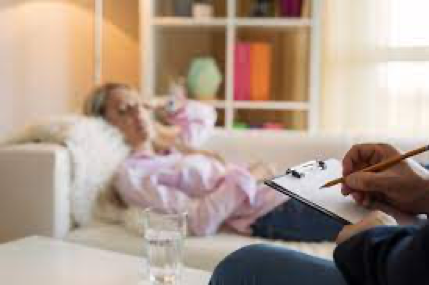 A woman is laying on a couch while a man writes on a clipboard.