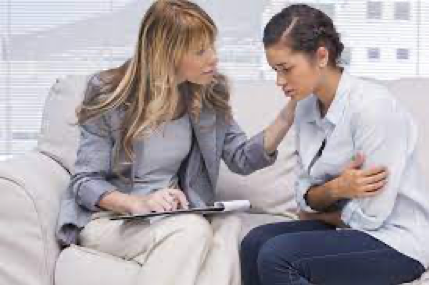 A woman is comforting another woman who is sitting on a couch.
