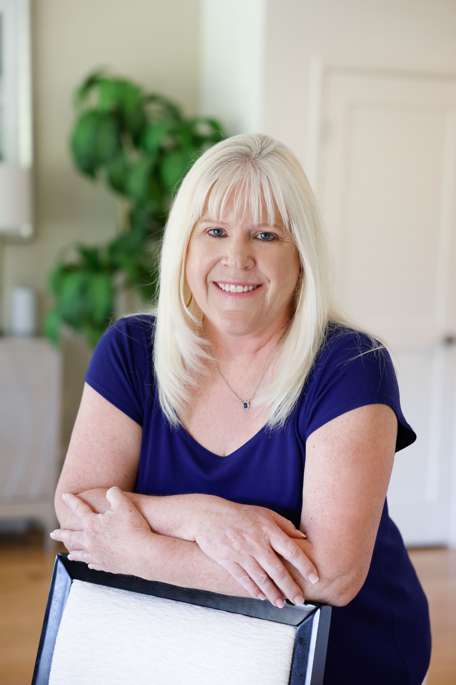 Kim Silverman in a blue shirt is leaning on a chair and smiling.