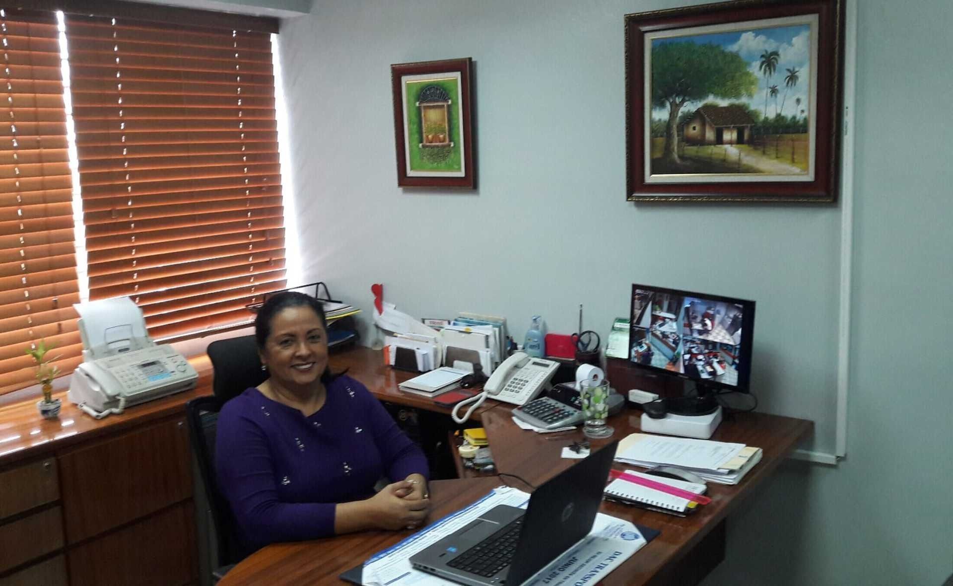 Una mujer está sentada en un escritorio con una computadora portátil encima.